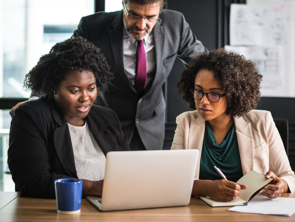 Man looking over shoulders of two women in the office