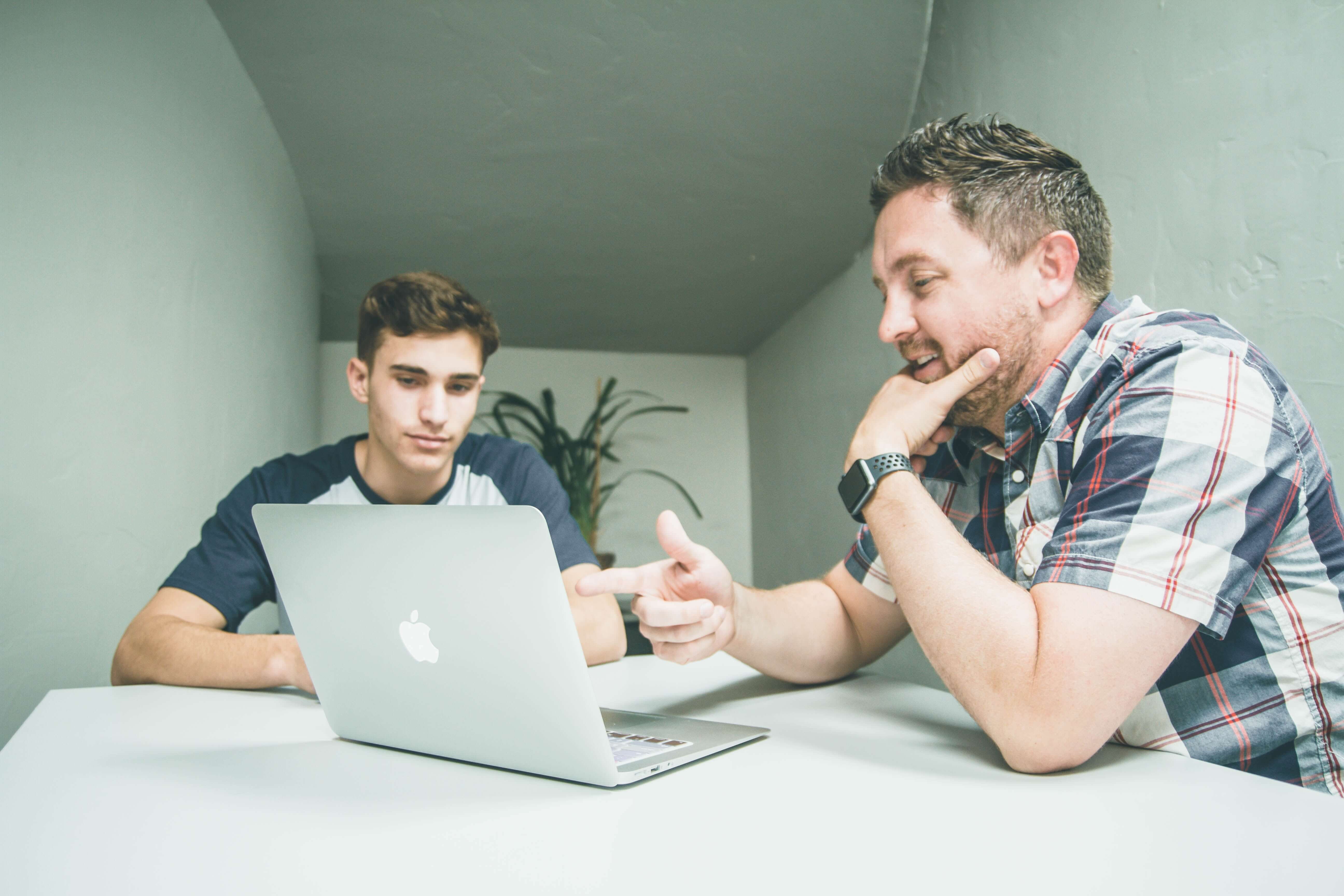 two men sitting around a macbook