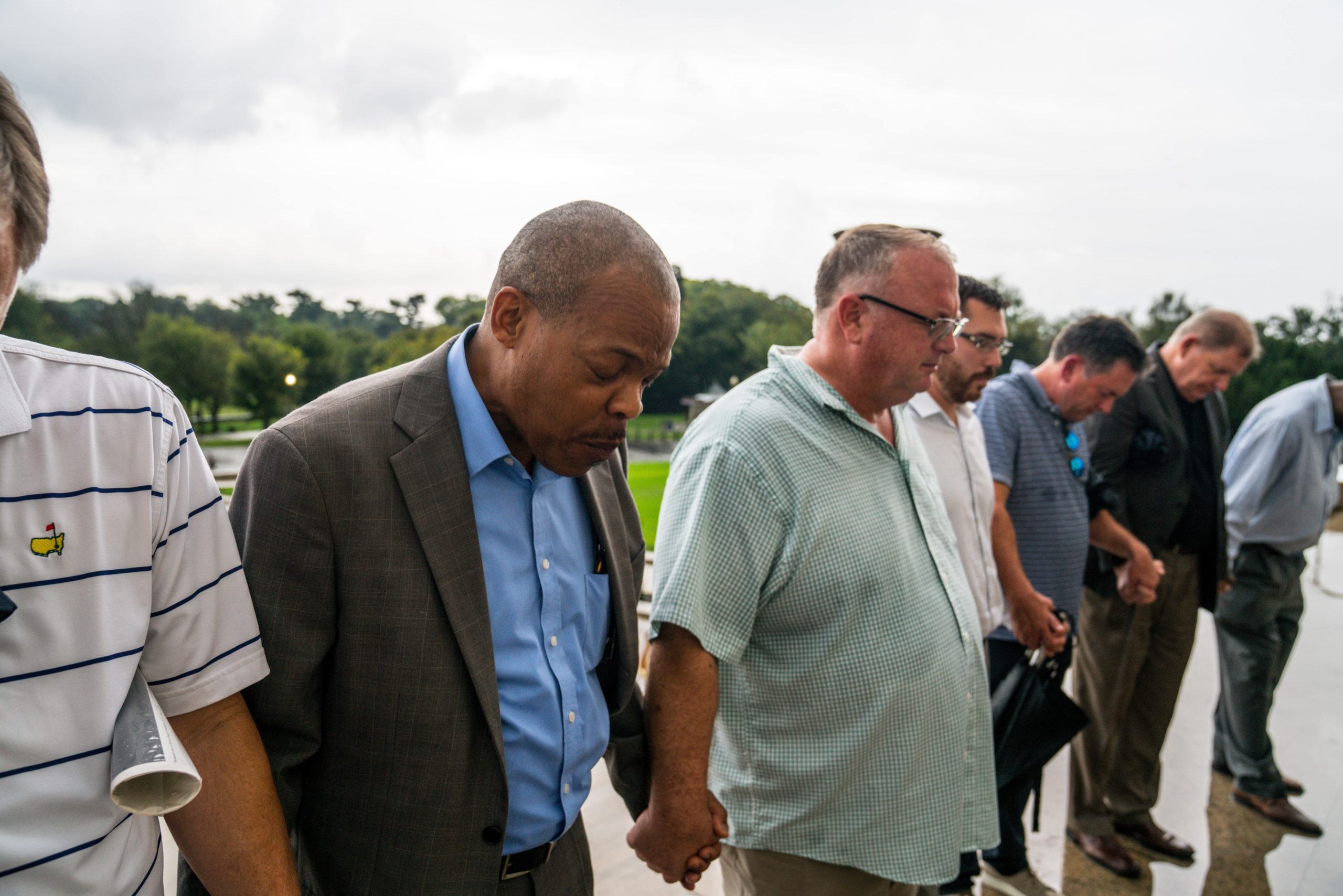 multiracial line of men holding hands and praying together