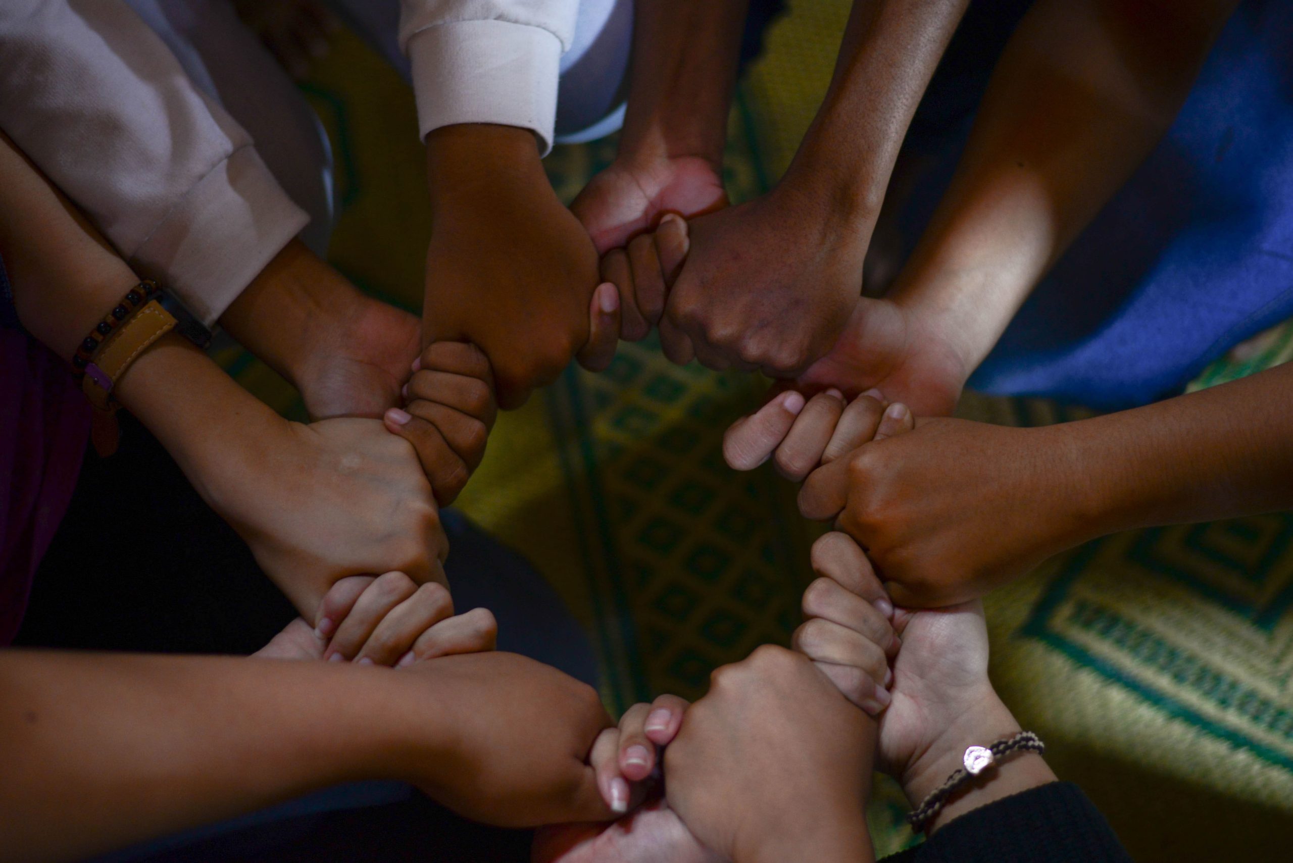 group of different colored hands holding one another in harmony