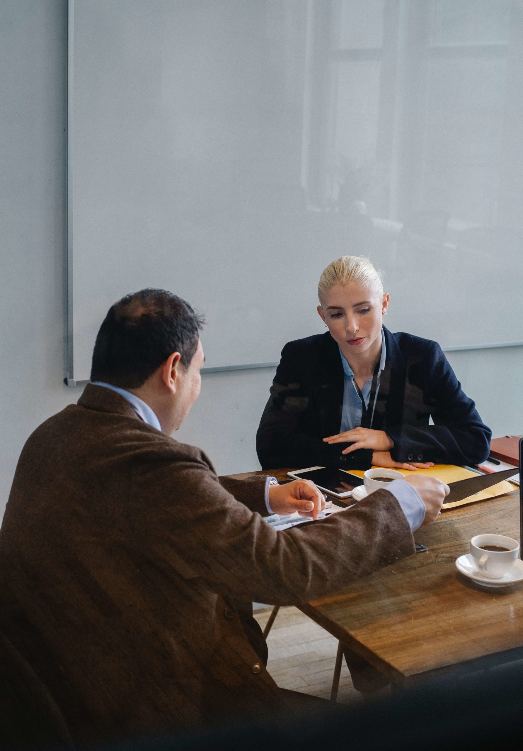 White woman with an Asian man at the conference table talking.